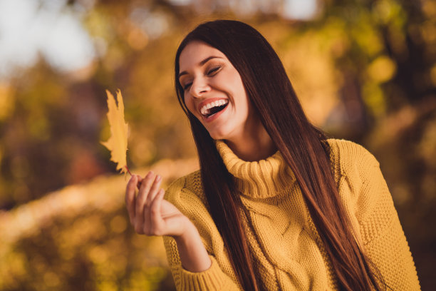 正面开朗的女孩享受休息放松秋天林地旅行看死黄色的枫叶笑穿毛衣的近距离照片图片下载