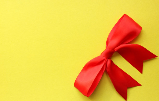 平铺漂亮的红色鲜艳的四廓缎带蝴蝶结黄色背景节日礼物。节日和包装。从以上观点。短打位于右下角。本空间图片下载