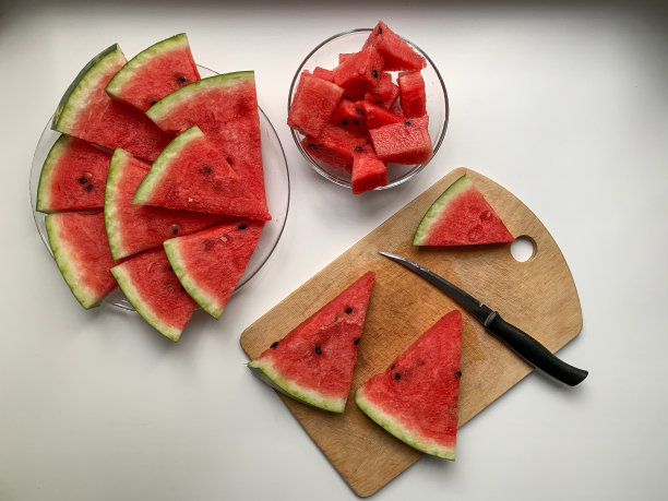 切西瓜的过程。新鲜的西瓜切片放在木板上，透明的盘子和切片的西瓜放在杯子里。从上面的照片。图片下载