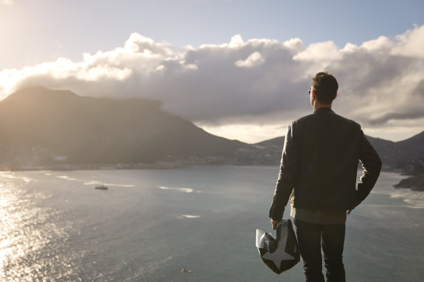 一个拿着摩托车头盔站在悬崖边上的男人图片下载