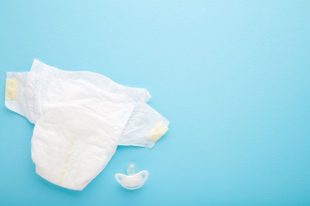 白色婴儿尿布和奶嘴在浅蓝色的桌子背景。柔和的颜色。特写镜头。文本的空位置。自顶向下的观点。图片下载