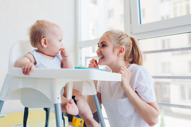 妈妈在家用水果喂小婴儿。家人一起吃饭。婴儿坐在儿童座椅上图片下载