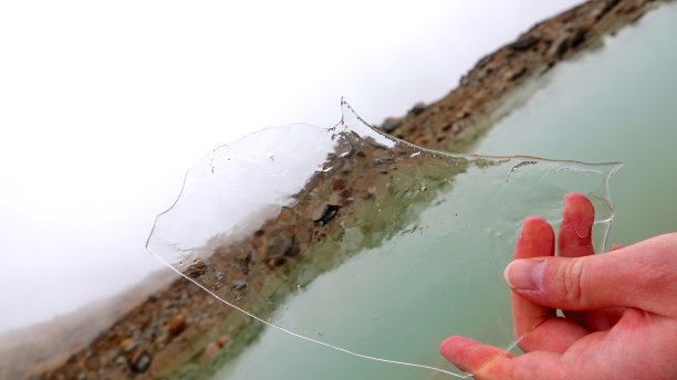 冬天寒冷的一只红色的手握着湖面上透明的浮冰。(图片显示的是意大利白云石山脉的佩奥冰川的情况。全球变暖正在融化那里的雪、冰和永久冻土。现在只剩下这个湖了。图片下载