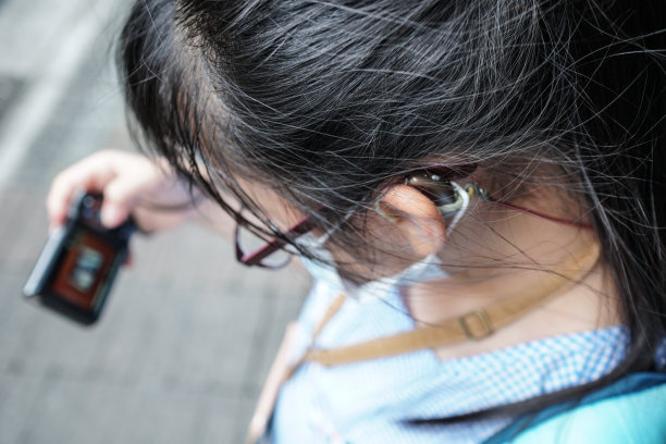 戴着助听器的失聪儿童。她正在用数码相机。在公共汽车站。字在右边。在看。图片下载