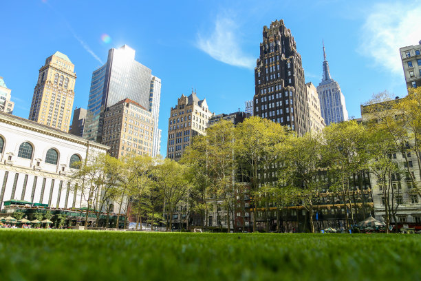 布莱恩特公园的春天。人们放松，绿色的草坪和树木，清澈的蓝天和摩天大楼的背景图片下载