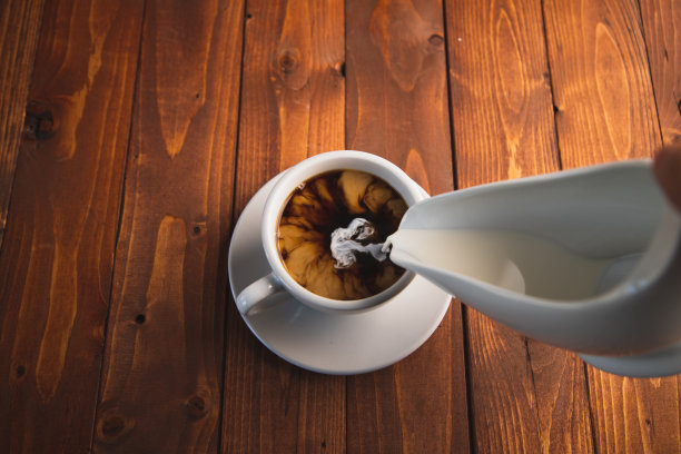 把奶油倒进白杯子里的黑咖啡里图片下载