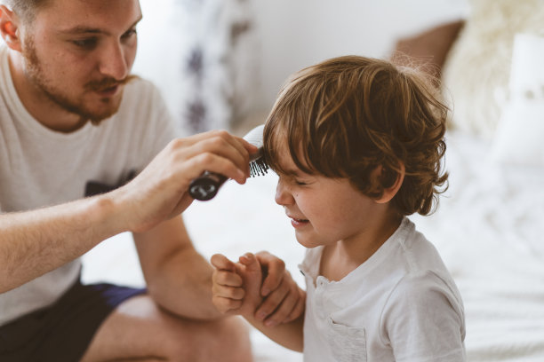 父亲在房间里给儿子剪头发。隔离期间的家人男性手中的剪刀和梳子图片下载