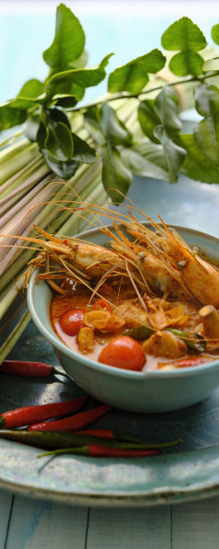 在国际上享有盛名的香辣泰式椰子汤“冬阴功”，以蓝色的碗搭配柠檬草、青柠叶和红辣椒，在蓝色的陶瓷盘子上，在蓝色的木制桌子的背景上。图片下载