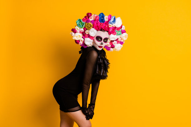 照片迷人的calavera卡特里娜手膝盖姿势调情死人僵尸穿黑色短迷你裙死亡嘉年华服装蕾丝手套玫瑰头带孤立黄色背景图片下载