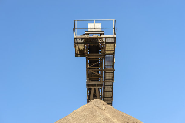 在水泥工业工厂的蓝天下，传送带上的碎石堆。图片下载