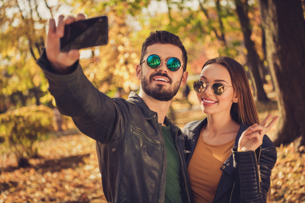 两人的照片学生女生男生在手机上自拍做v手势在秋天九月季节公园戴眼镜夹克图片下载
