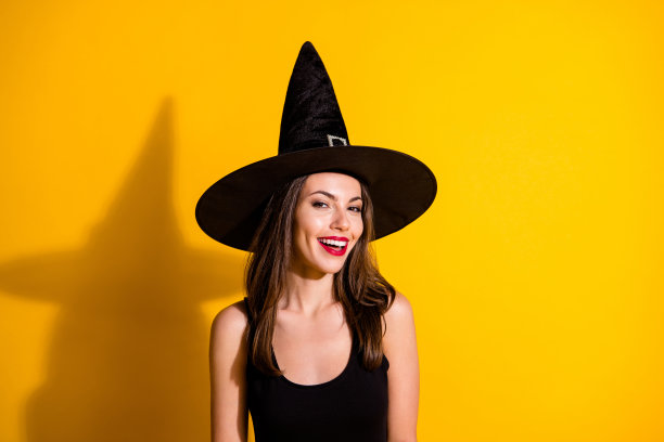 照片迷人的漂亮的年轻女士微笑，红色明亮的口红，挑逗的看吸引英俊的男朋友穿黑色女巫服装锥头孤立的黄色背景图片下载