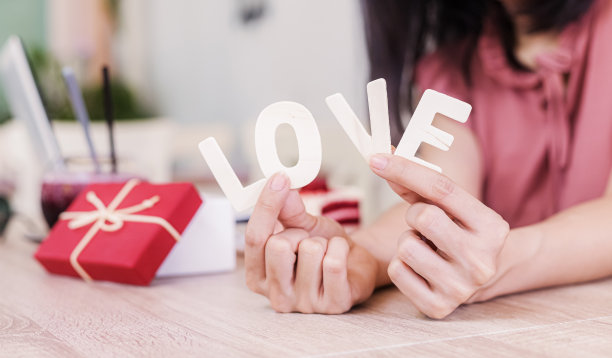 手牵着爱的字靠近礼品盒放在桌子上。图片下载