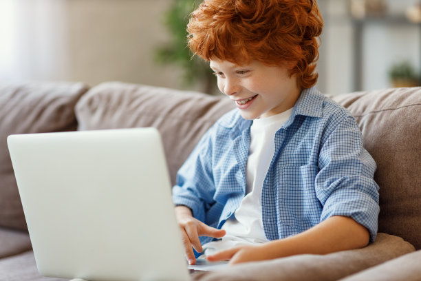 快乐的姜男孩在沙发上用平板电脑图片下载