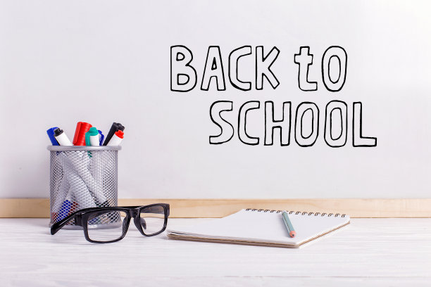 马克笔，眼镜，笔记本，铅笔和白板。白板上的题词是“回到学校”。图片下载
