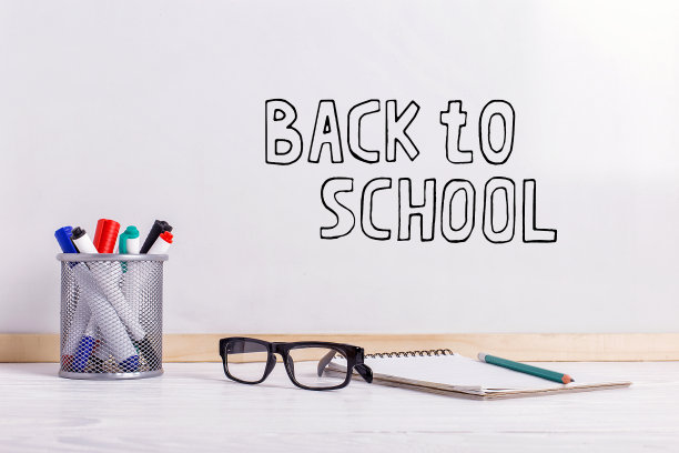 马克笔，眼镜，笔记本，铅笔和白板。白板上的题词是“回到学校”。图片下载