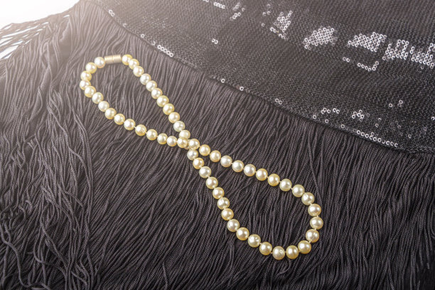 黑色小礼服上的珍珠首饰。盖茨比或芝加哥的时尚装扮。豪华白色项链。为派对做准备。优雅的女人礼物。背光图片下载