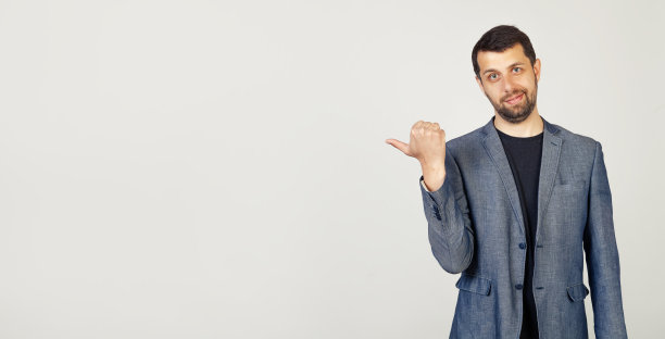 一个留着胡子的年轻人面带微笑，用他的拇指指着一边的一个广告位置，看这里，在孤立的背景上图片下载