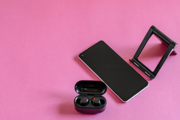 平放照片与手机，无线耳机和手机支架在粉红色的背景。现代技术的概念。图片下载