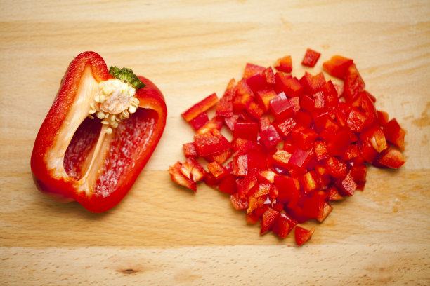 一半红甜椒和切碎的辣椒放在木砧板上。图片下载