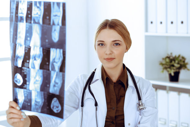 一位女医生在医院窗户附近检查x光照片。在工作中的外科医生或整形外科医生医疗保健理念。理疗师穿的卡其色衬衫很好看图片下载