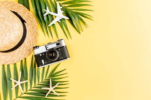 旅行者配件概念上的黄色背景。复古相机，模型飞机，飞机，草帽和热带棕榈叶图片下载
