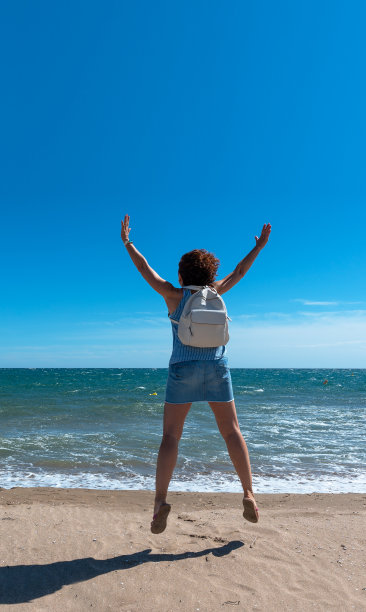 在一个阳光明媚的日子里，一个女人在海滩上高兴地跳着。本空间图片下载
