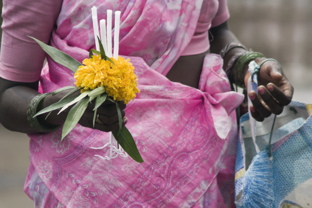 一个女人的手拿着鲜花和蜡烛在街上出售的特写。图片下载