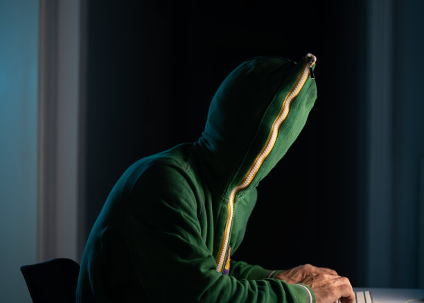戴拉链帽衫和口罩的男子在黑暗中使用笔记本电脑进行黑客攻击图片下载