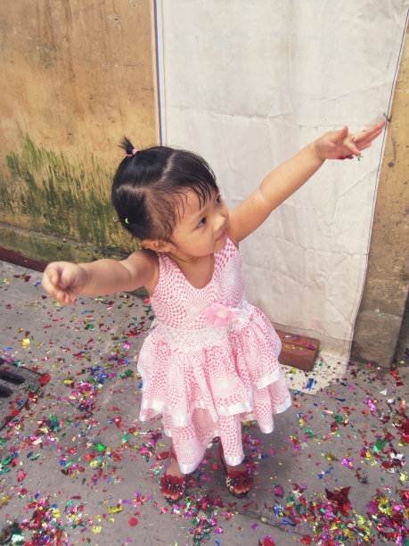 一个可爱的小女孩穿着粉红色的裙子在街上扬起她的手，脸上洋溢着快乐图片下载