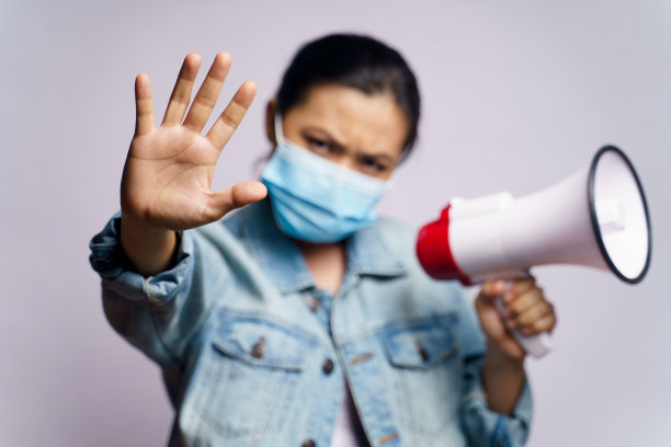 亚洲妇女戴着保护面罩，用扩音器在白色背景下喊叫。图片下载