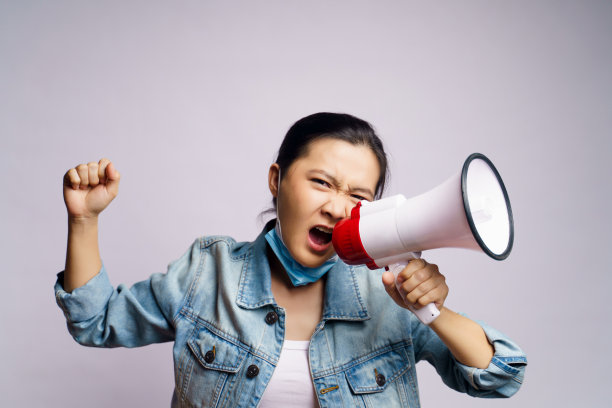 亚洲妇女戴着保护面罩，用扩音器在白色背景下喊叫。图片下载