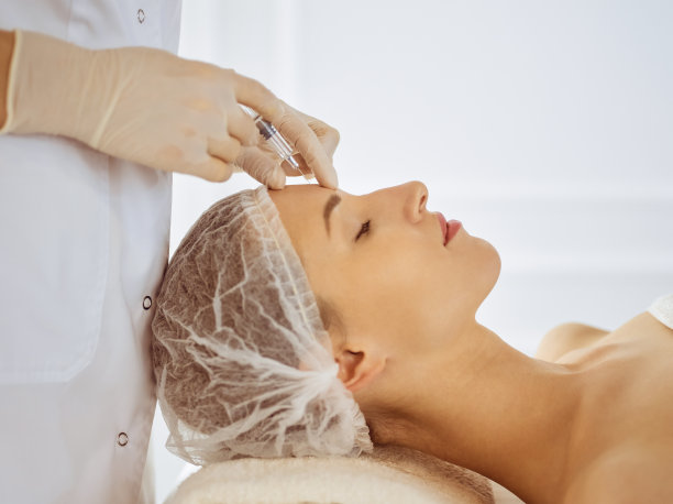 闭着眼睛接受美容注射的美女。美容师医生用注射器给女性脸部做美容手术。美容医学和外科概念图片下载