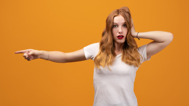 漂亮的女孩与波浪形红发惊讶和指向一边的手指，显示副本空间为您的信息图片下载