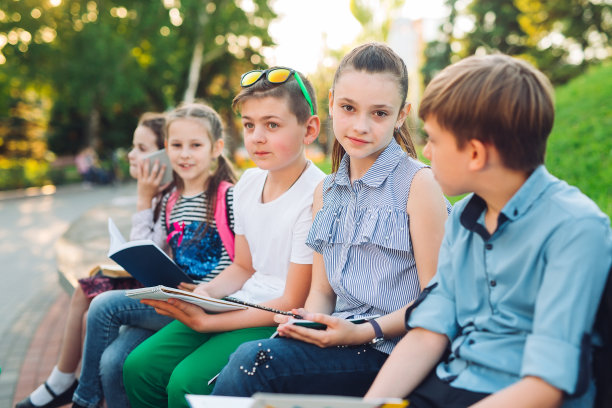 快乐的同学们的肖像。同学们坐在城市公园的木凳上看书，在阳光明媚的日子学习。图片下载