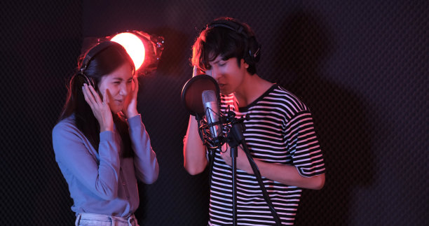 年轻的亚洲有吸引力的音乐家一起在现代录音棚录制新歌快乐歌唱。两个年轻人一起工作的新音乐专辑在工作室的黑暗背景。图片下载