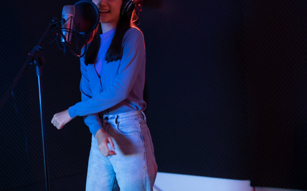 年轻的亚洲女子有吸引力的音乐家快乐歌唱录音新歌在现代录音室。在黑暗的背景下，美丽的女性在录音室的麦克风旁工作和唱歌。图片下载