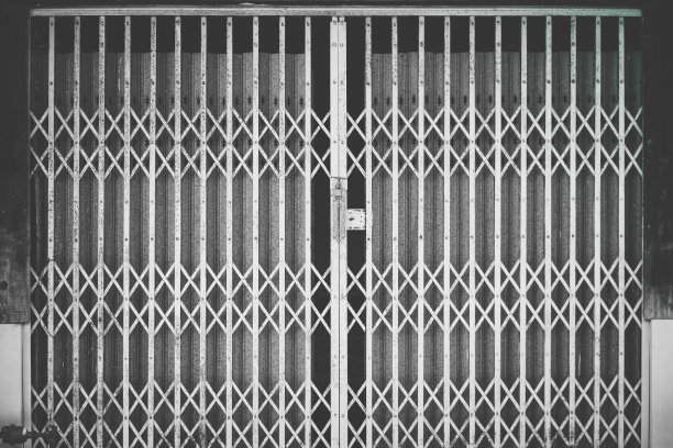 古老的钢制门。商店或工业建筑物上的百叶窗。陈旧生锈的金属卷帘门图案背景和纹理-复古风格-黑白滤镜处理。图片下载