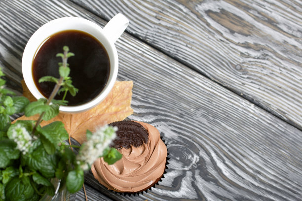 奶油芝士奶油巧克力纸杯蛋糕。旁边是一杯咖啡和干枫叶。有一个罐子，里面放着盛开的薄荷枝。图片下载