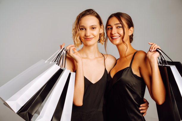 年轻女性朋友拿着黑白包包在灰色背景下摆姿势。图片下载