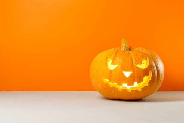 橙色背景下发光的万圣节南瓜。图片下载