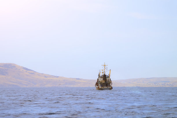 一艘旧渔船沿着多山的海岸航行，拉着网图片下载