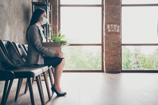 严重女孩失业需要新职业的身长侧面照片坐椅子、牌、箱等招聘、hr面试、穿夹克、戴医用口罩在工作场所工作站图片下载
