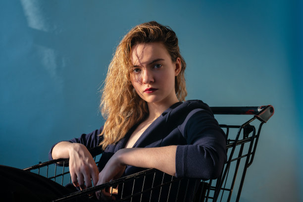 女孩在一件夹克运动鞋西装在一个黑色的购物车在一个蓝色的背景图片下载