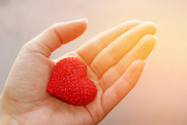 在一个女人的手里用棉线钩出了红色的心。是爱和温柔的象征。图片下载