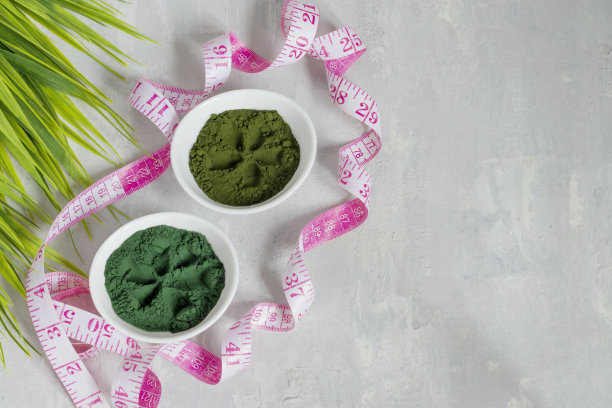 小球藻和螺旋藻粉在光线背景下。绿色超级食物为素食者排毒。健康的生活方式的概念。测量数字的卷尺。本空间图片下载