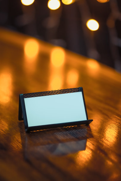 空的卡片持有人木制桌子模拟的名片，白色的名片模拟标签卡在模糊的灯光背景图片下载