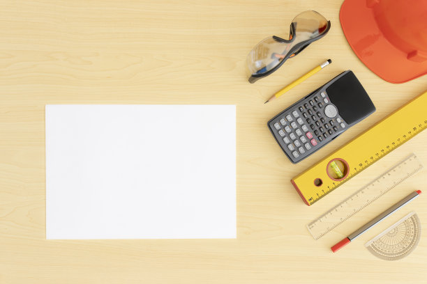 俯视图工程师办公桌有浅棕色的木质纹理卷回家平面图和工具，卷尺，计算器，带拷贝的安全帽空间。房子平面图上有木桌，建筑师有安全眼镜和工作场所图片下载