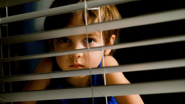 一个沉思的小男孩在夜晚透过窗户向外偷看图片下载