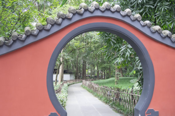 一堵红墙的圆形入口通向一个有许多树木和竹子的中国花园图片下载